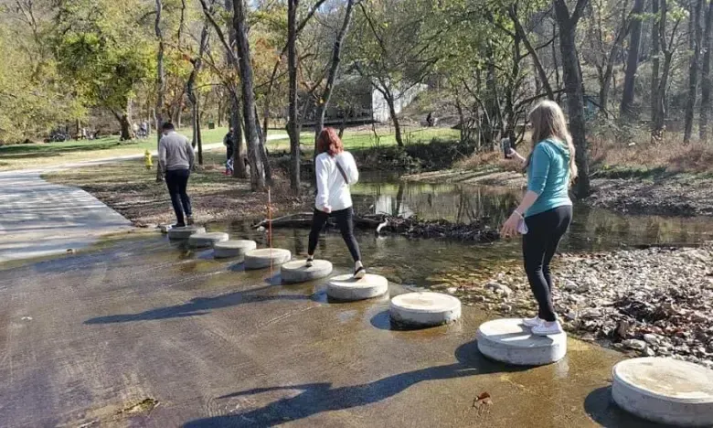 Three people crossing a stream on stone steps in a wooded area.