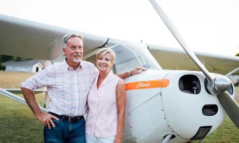 Older couple smiling beside a small airplane outdoors.