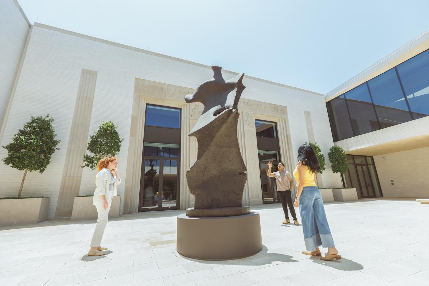 Four people admire a sailboat sculpture in a sunny white courtyard.