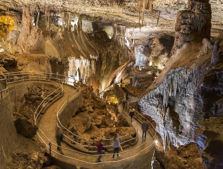Cave interior with pathway, rock formations, and tourists walking.