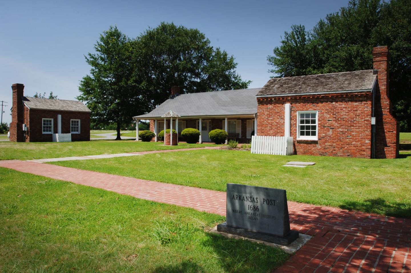 Historical brick buildings with green lawn and pathway, under a blue sky.