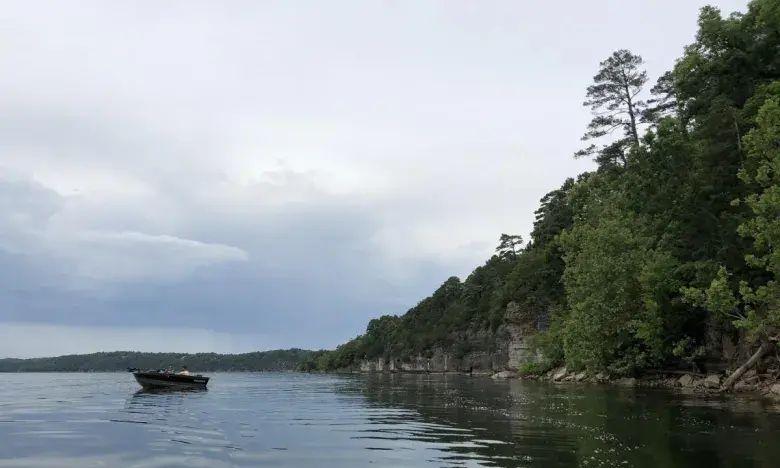 Calm lake with a boat near a tree-lined shore under a cloudy sky.