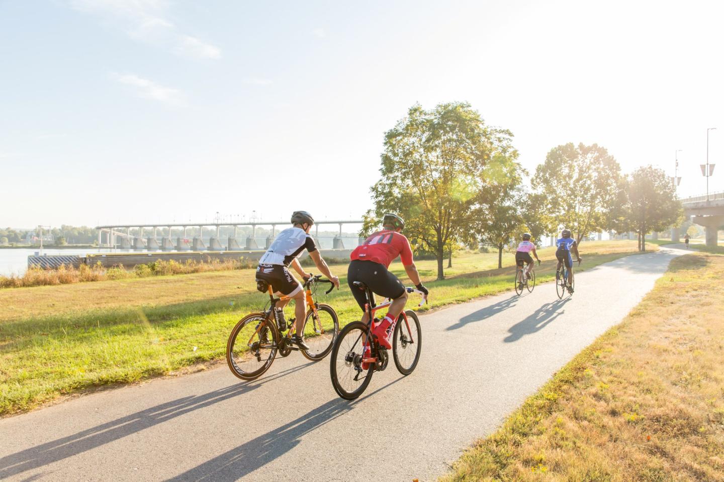 Cyclists riding on a sunny riverside path.