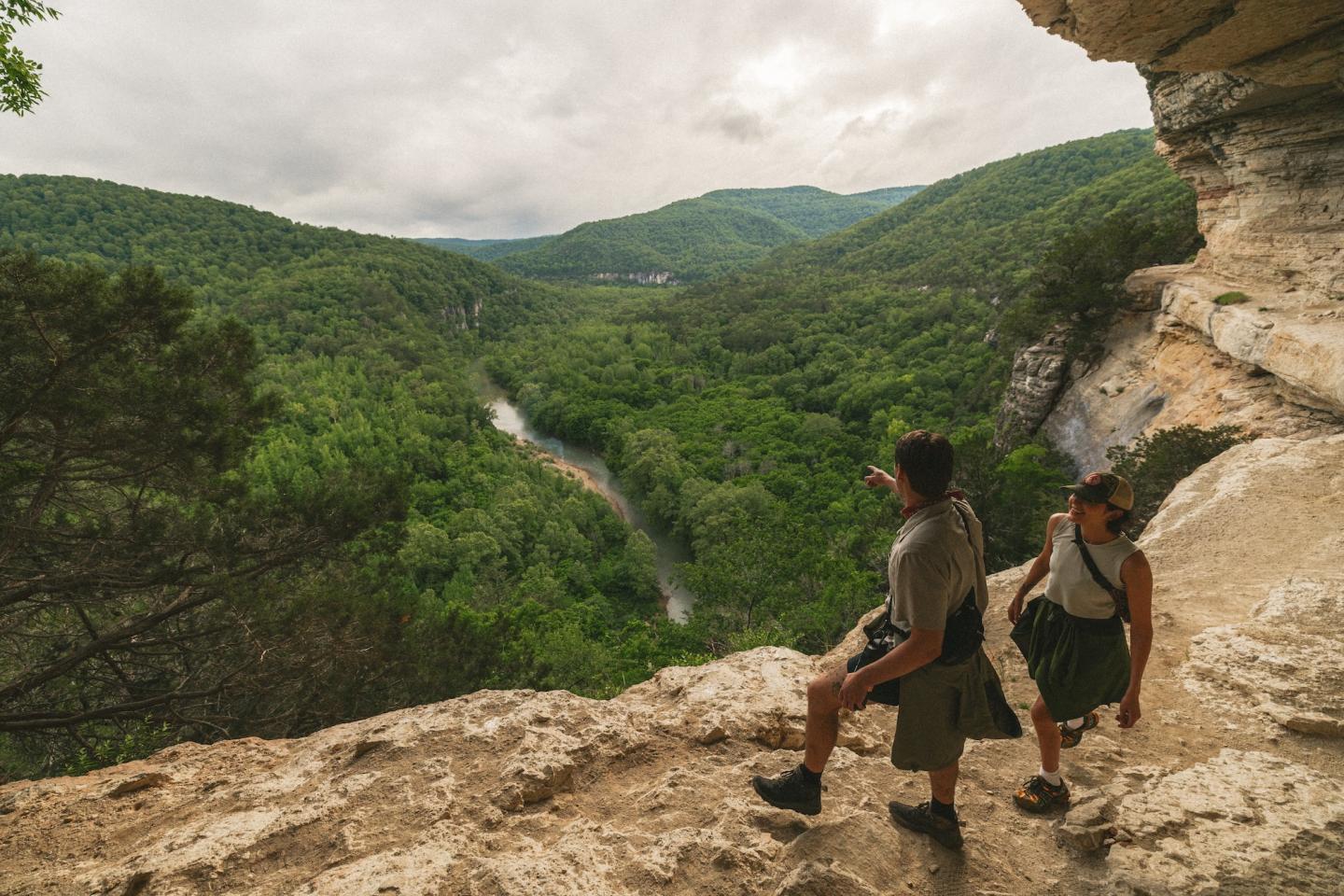 Two hikers overlooking a lush green valley with a winding river.