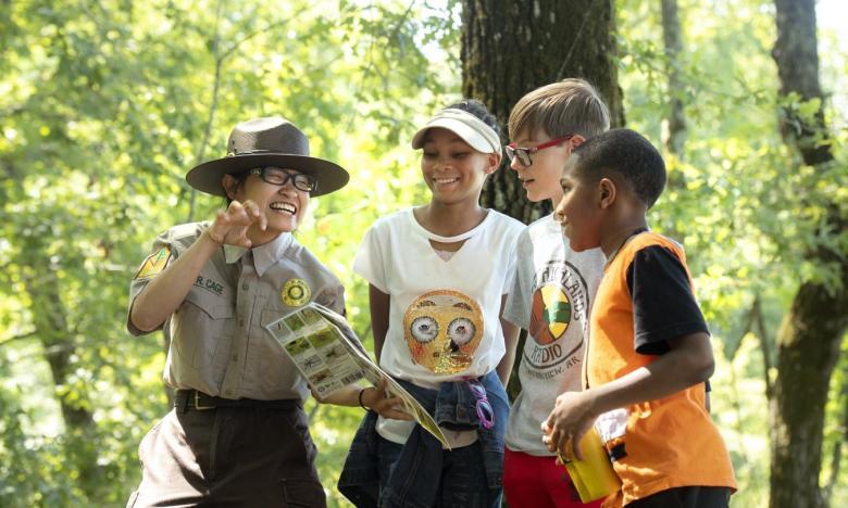 Park ranger guides three kids through a forest, showing a map.