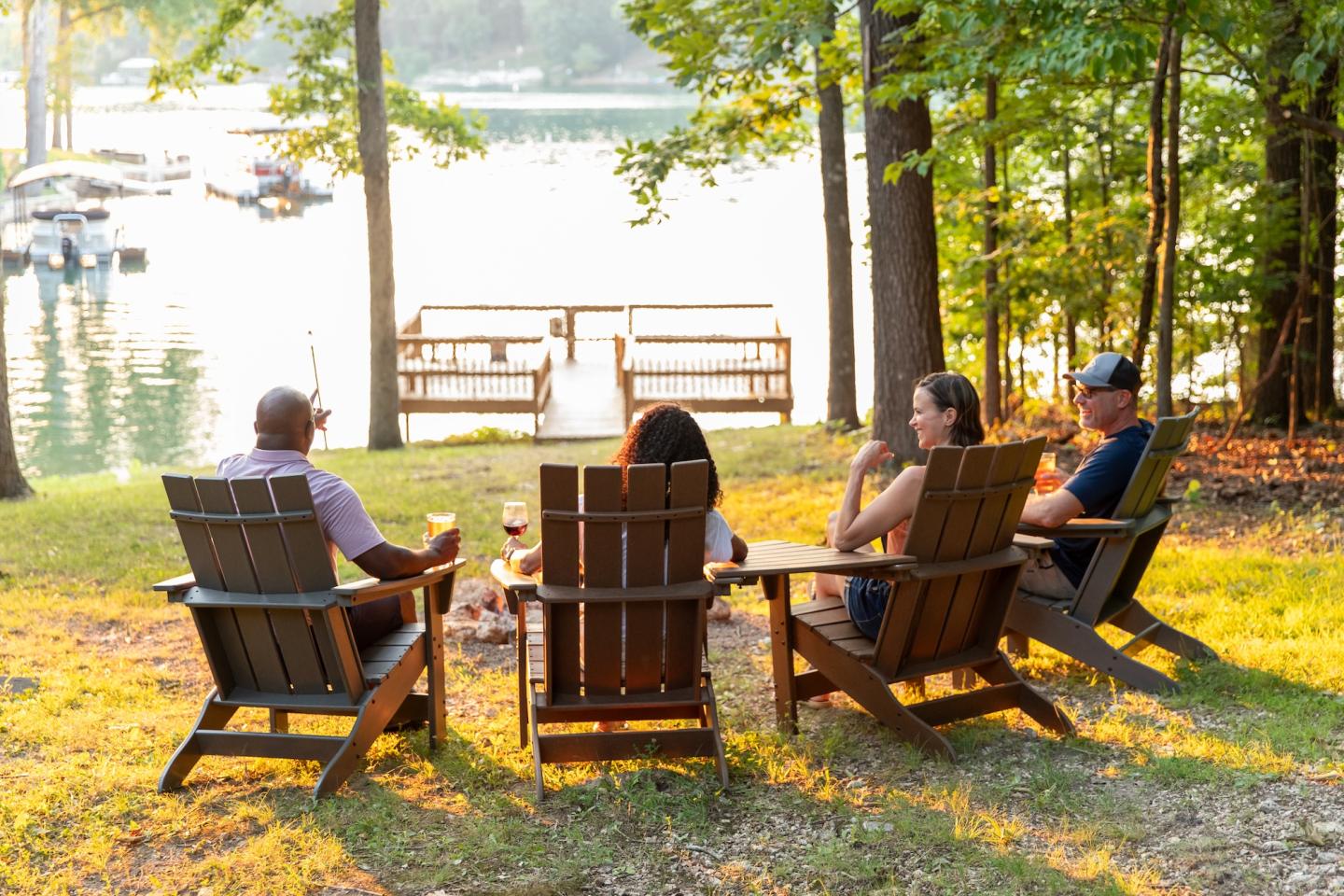 Four people sitting in chairs by a forested lake, enjoying a serene view.