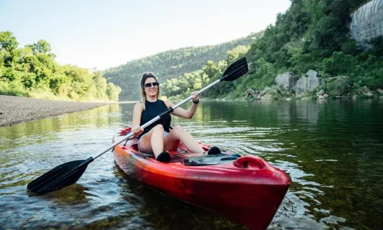 Woman kayaking on a river surrounded by lush green hills.