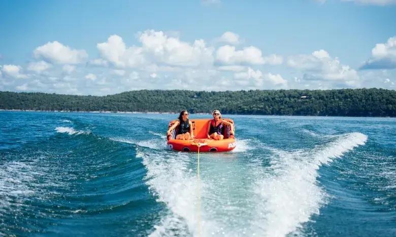 Two people enjoy tubing on a lake under a cloudy blue sky.