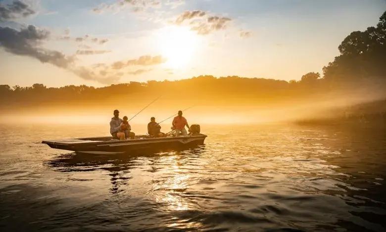 Boat with three people fishing on a misty lake at sunrise.