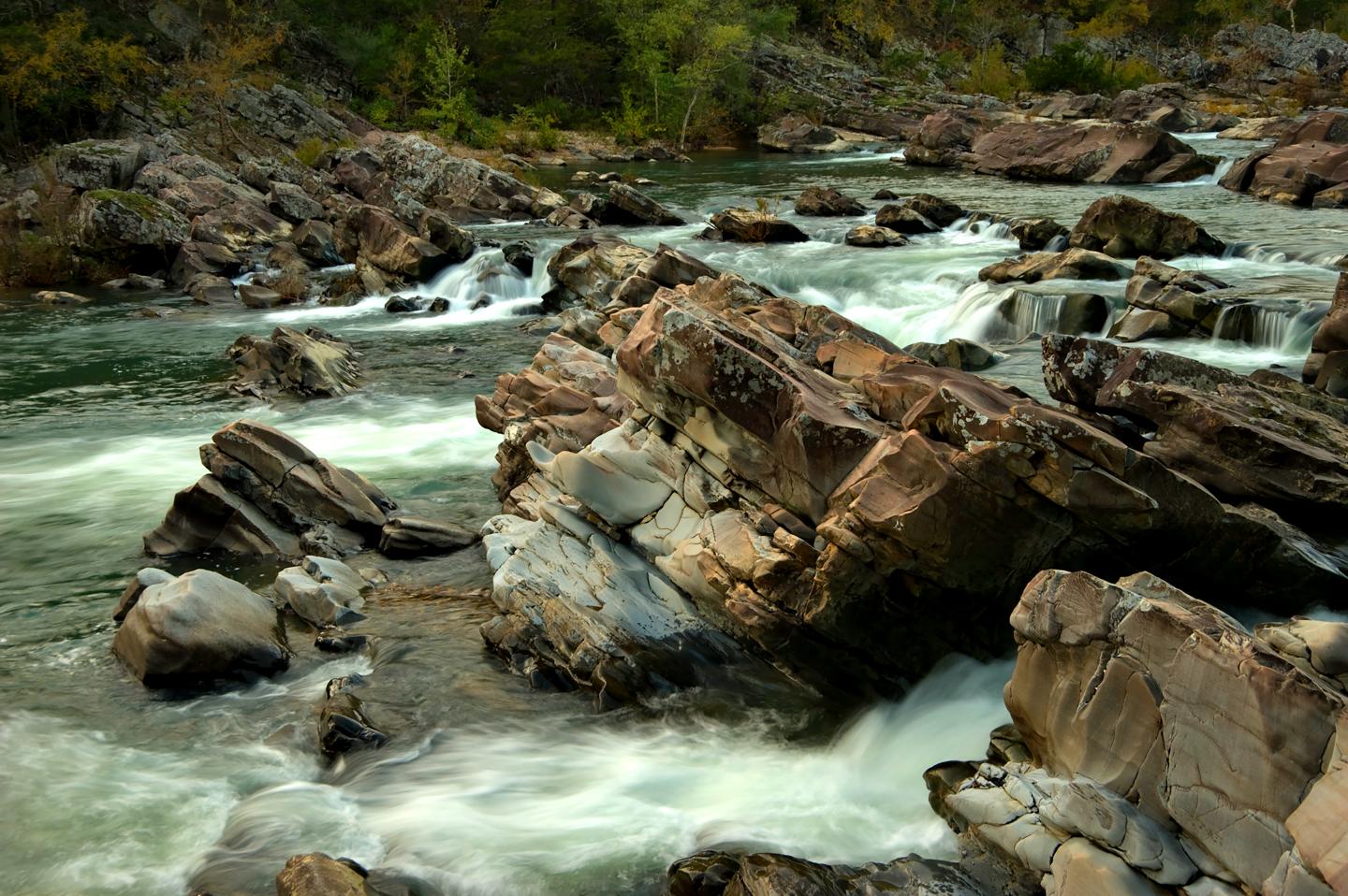 Rocky river with flowing water and greenery in the background.