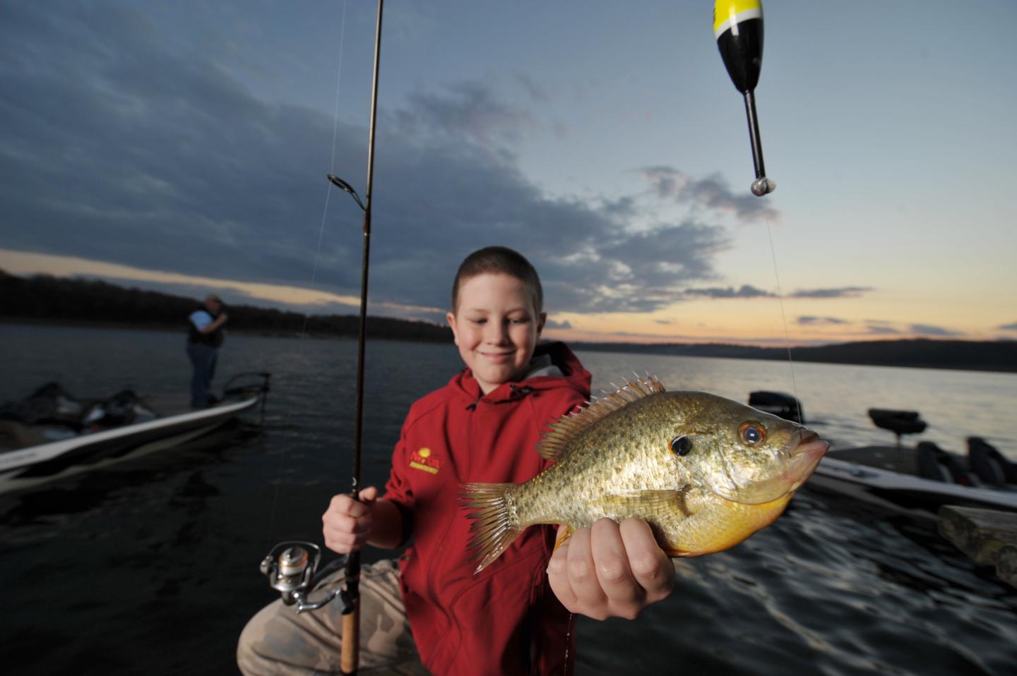 Boy holding a fish at sunset on a dock.