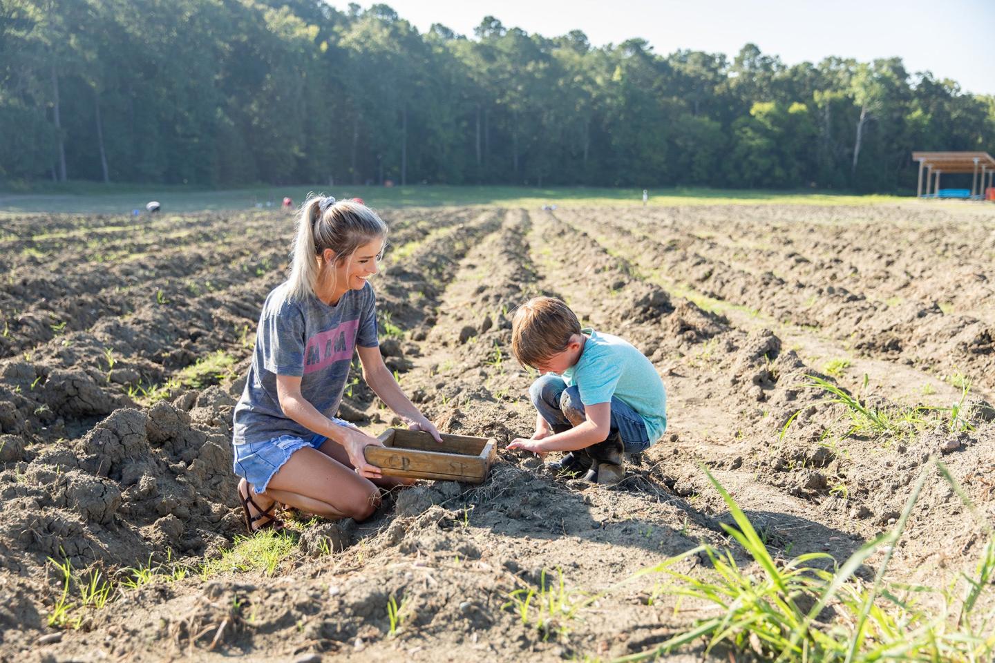 Woman and child kneeling in a field, examining the soil on a sunny day.