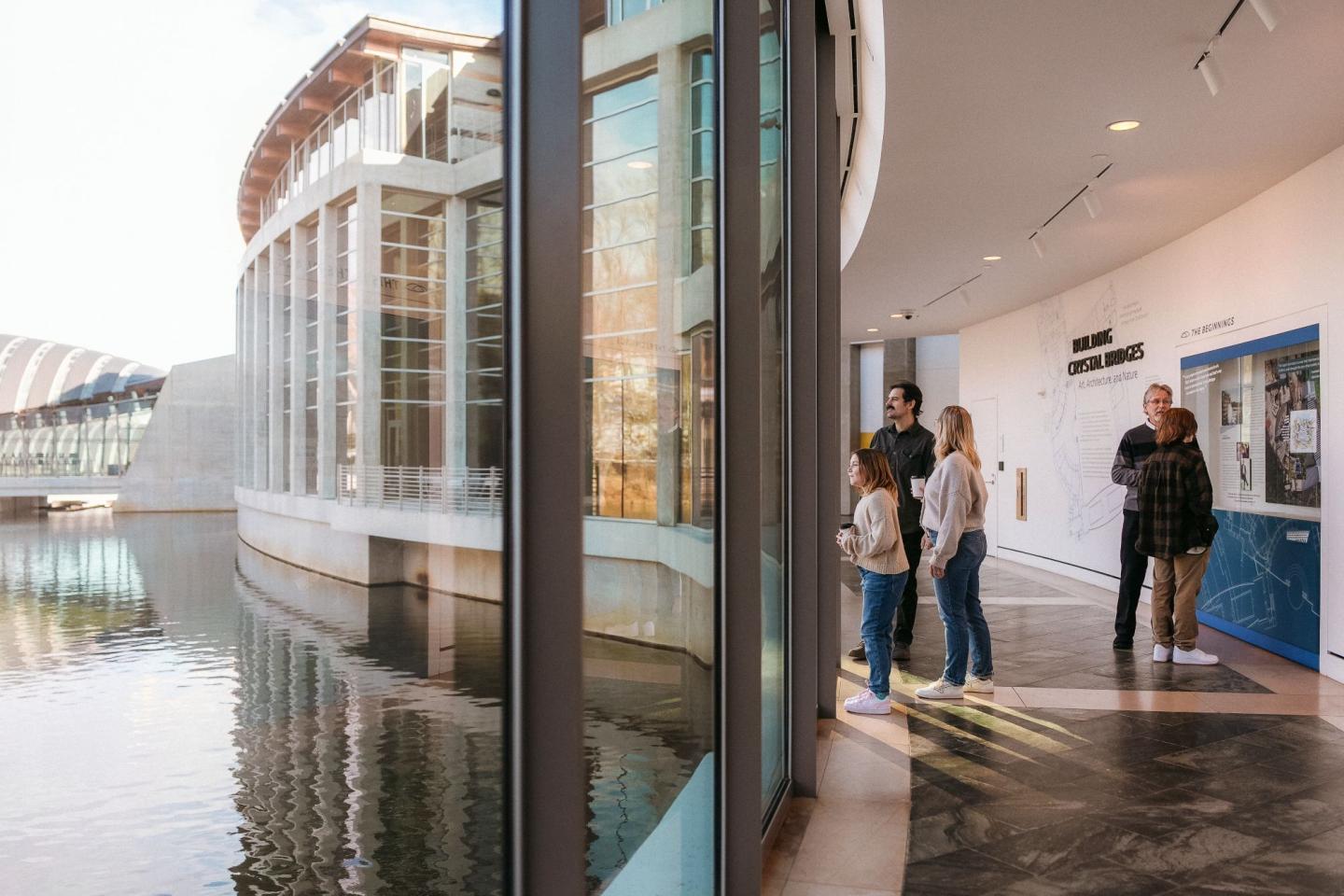 Visitors inside a modern art museum, near large windows overlooking water.