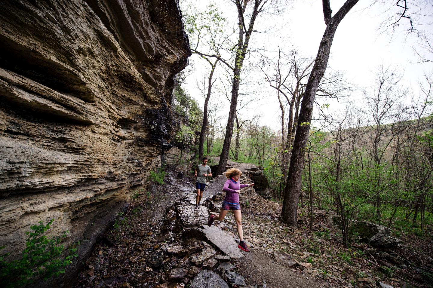 Hikers on a rocky trail by a cliff, surrounded by trees.