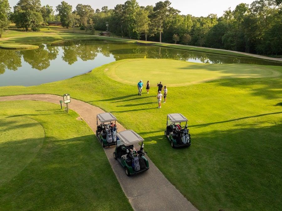 Golf course with carts, players near green, and lake reflecting trees.