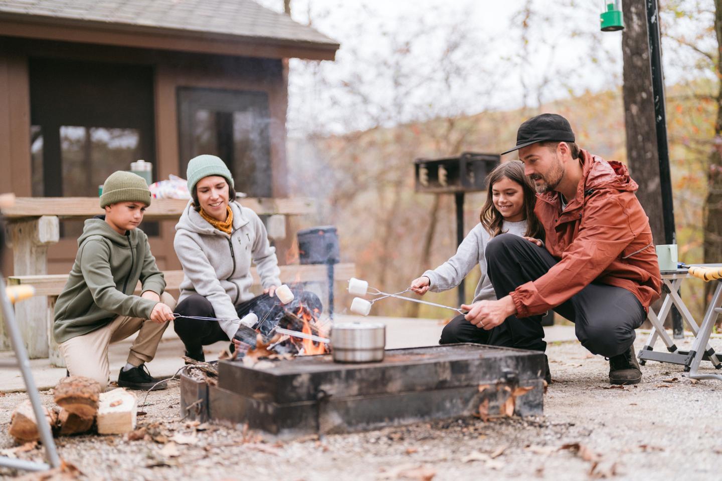 Family roasting marshmallows over a campfire in the woods.