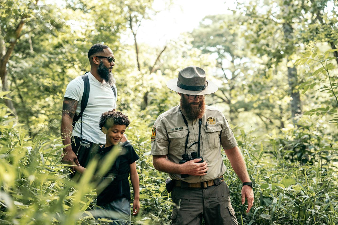 A park ranger leads a man and child through a lush forest.