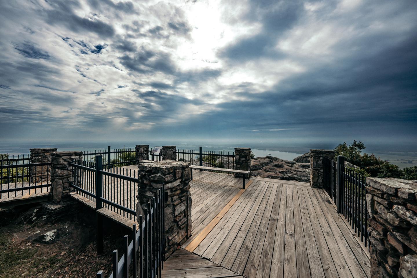 Wooden boardwalk with stone railings under a cloudy sky overlooking the sea.