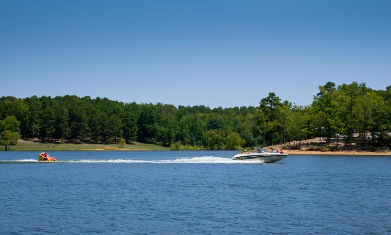 Speedboat on a lake, towing a person on an inflatable. Forest in the background.