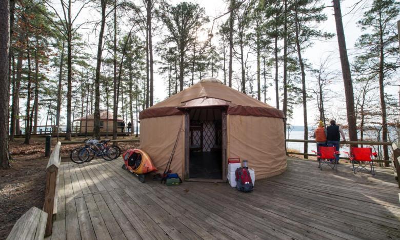 Yurt on a wooden deck surrounded by tall trees, with bicycles and luggage nearby.