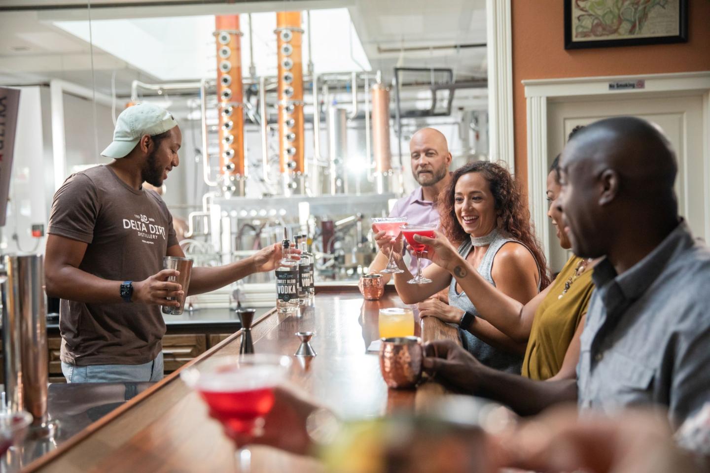Bar setting, bartender serves drinks to diverse, smiling patrons.
