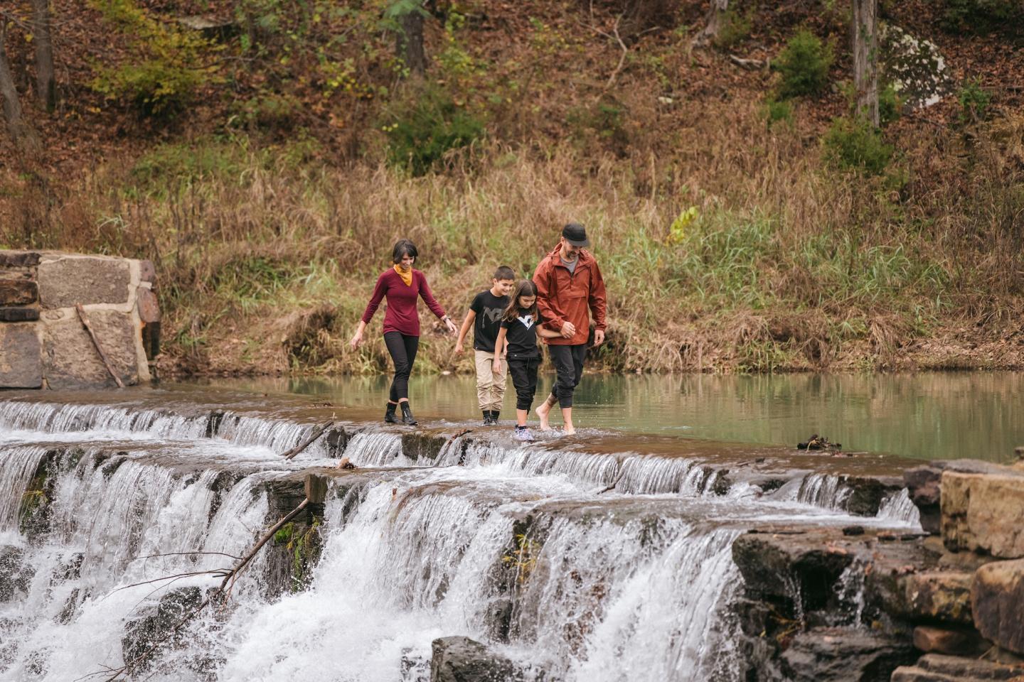 Family walking across a waterfall, surrounded by trees and greenery.