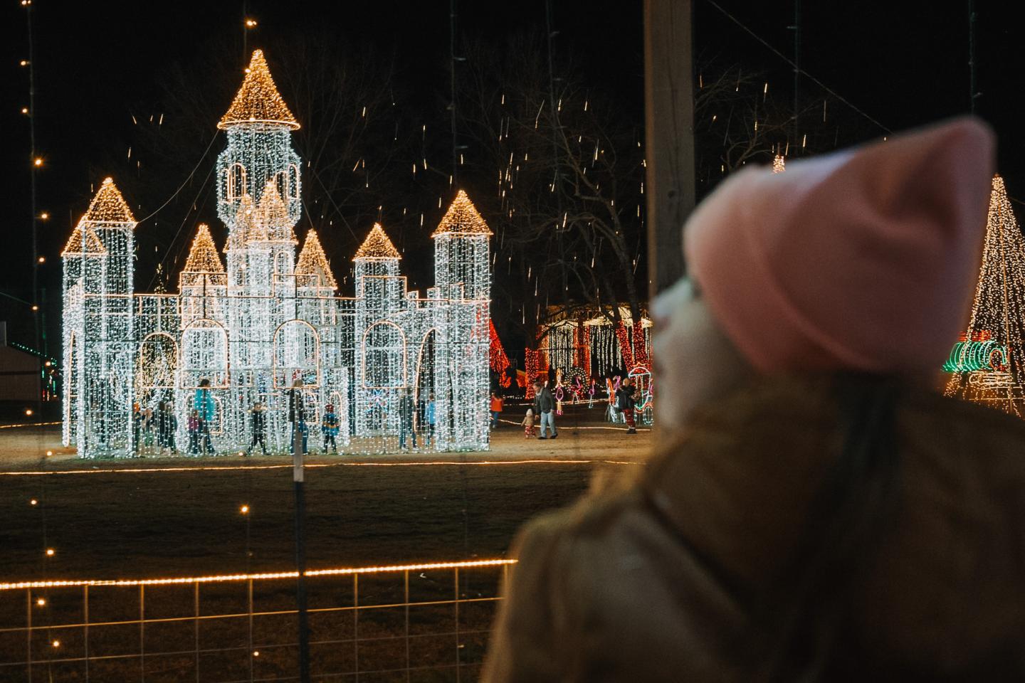 Child in pink hat admiring illuminated castle at night.