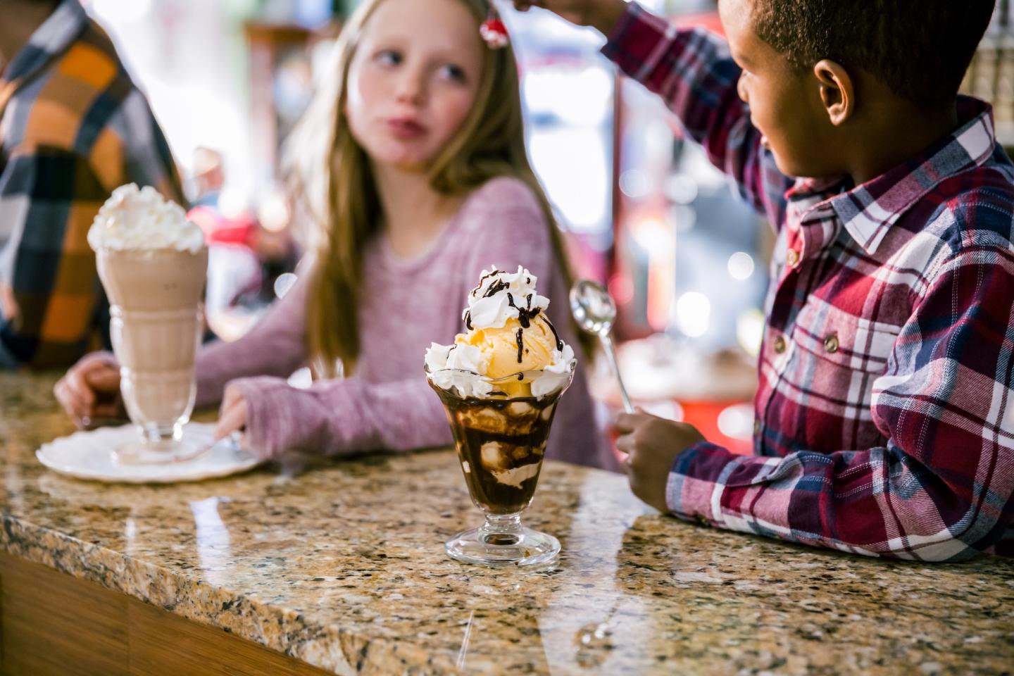 Kids enjoying ice cream sundaes at a counter.