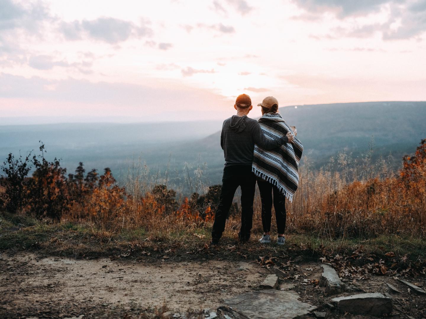 Couple embraces, overlooking a scenic sunset landscape.