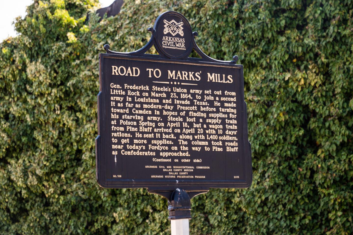 Historical plaque titled "Road to Marks Mills" with text, set against greenery.