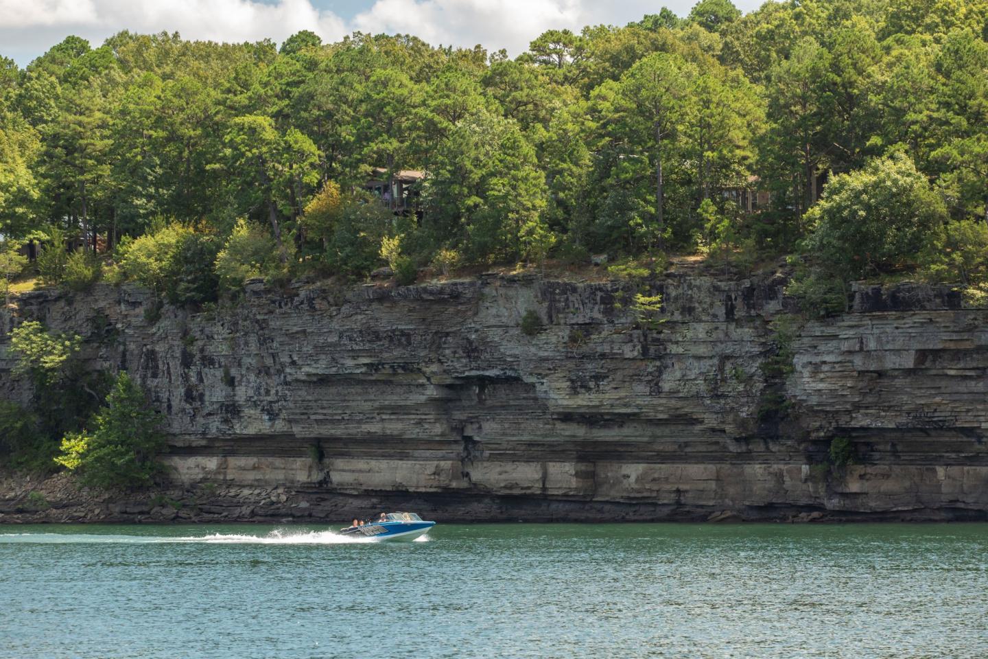 Speedboat on a lake with tall, tree-covered cliffs in the background.