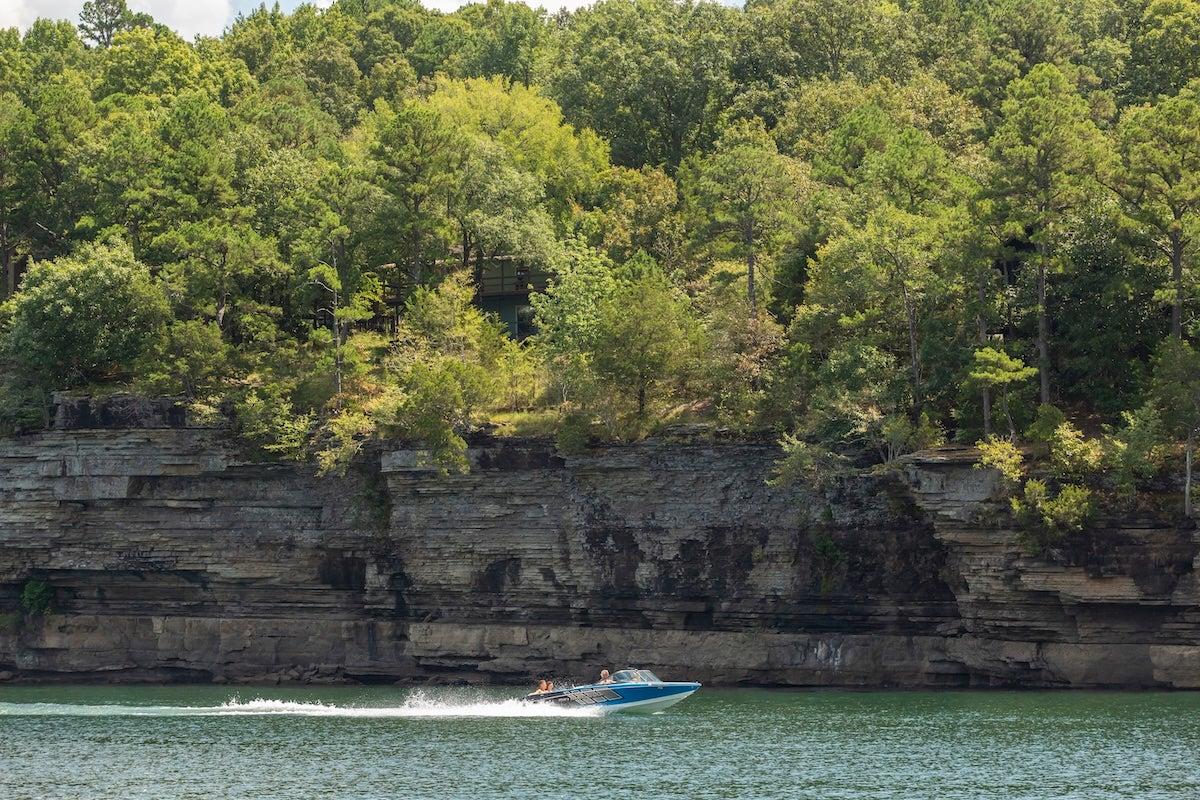 Speedboat on a lake with rocky shoreline and lush green trees.