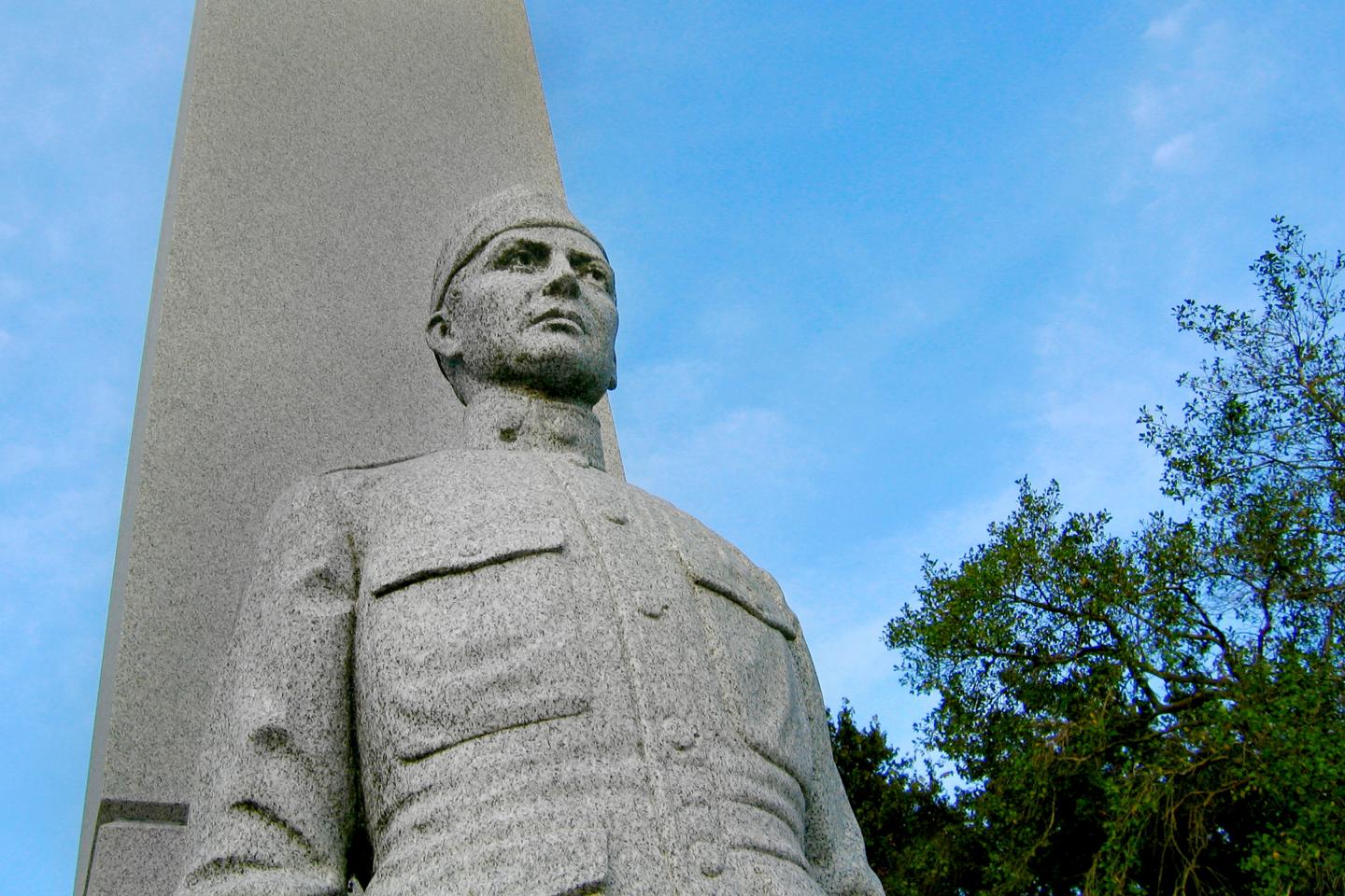 Statue of a soldier in uniform with trees in the background.