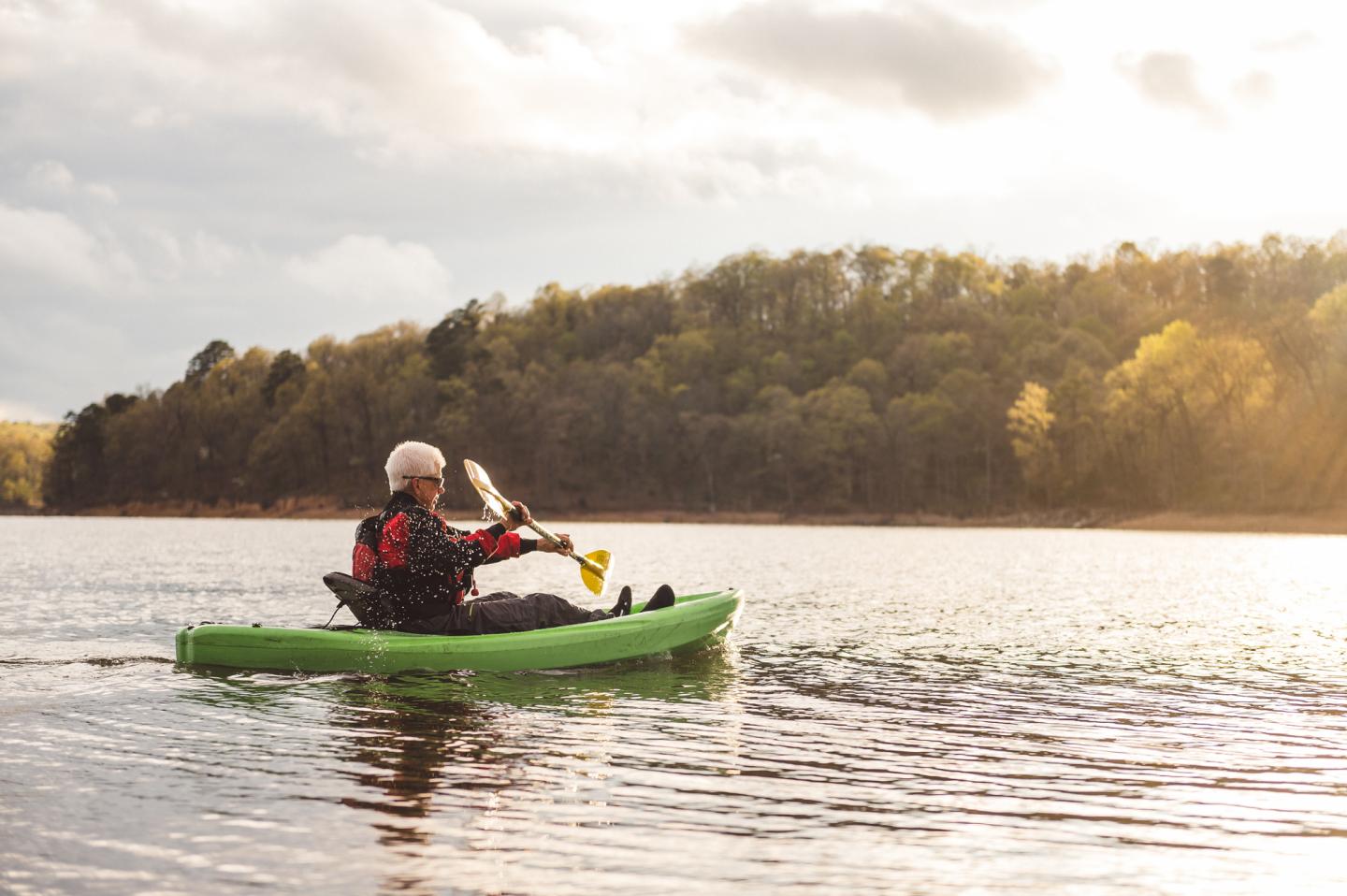 Kayaker paddling on a calm lake under a cloudy sky.