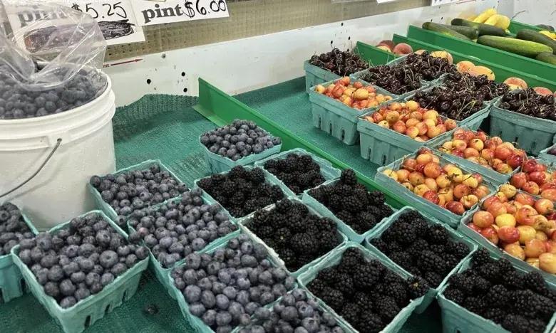 Berries and fruits in baskets at a market, with blueberries, blackberries, and peaches.