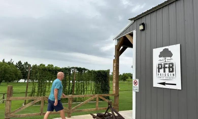 Man walking near a gray barn under a cloudy sky.