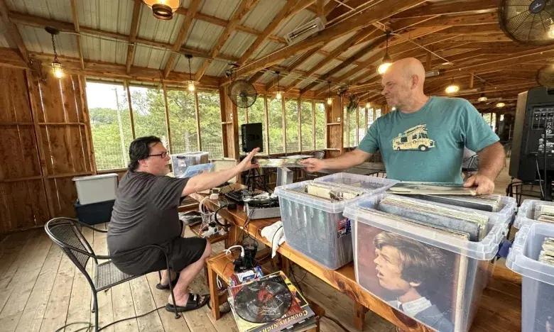 Two people exchanging vinyl records in a wooden cabin setting.