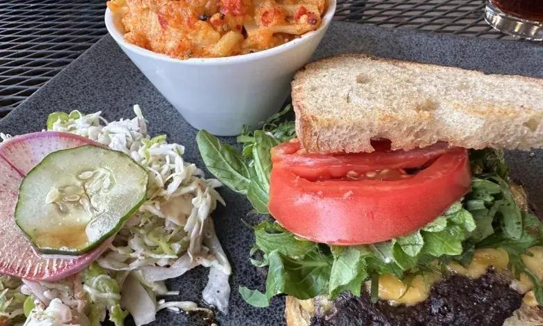 Burger with lettuce, tomato, cheese, side of pasta, and salad with cucumber.