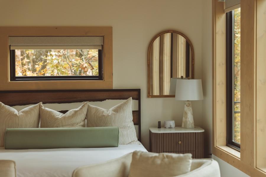 Cozy bedroom with large bed, neutral tones, arched mirror, and natural light.