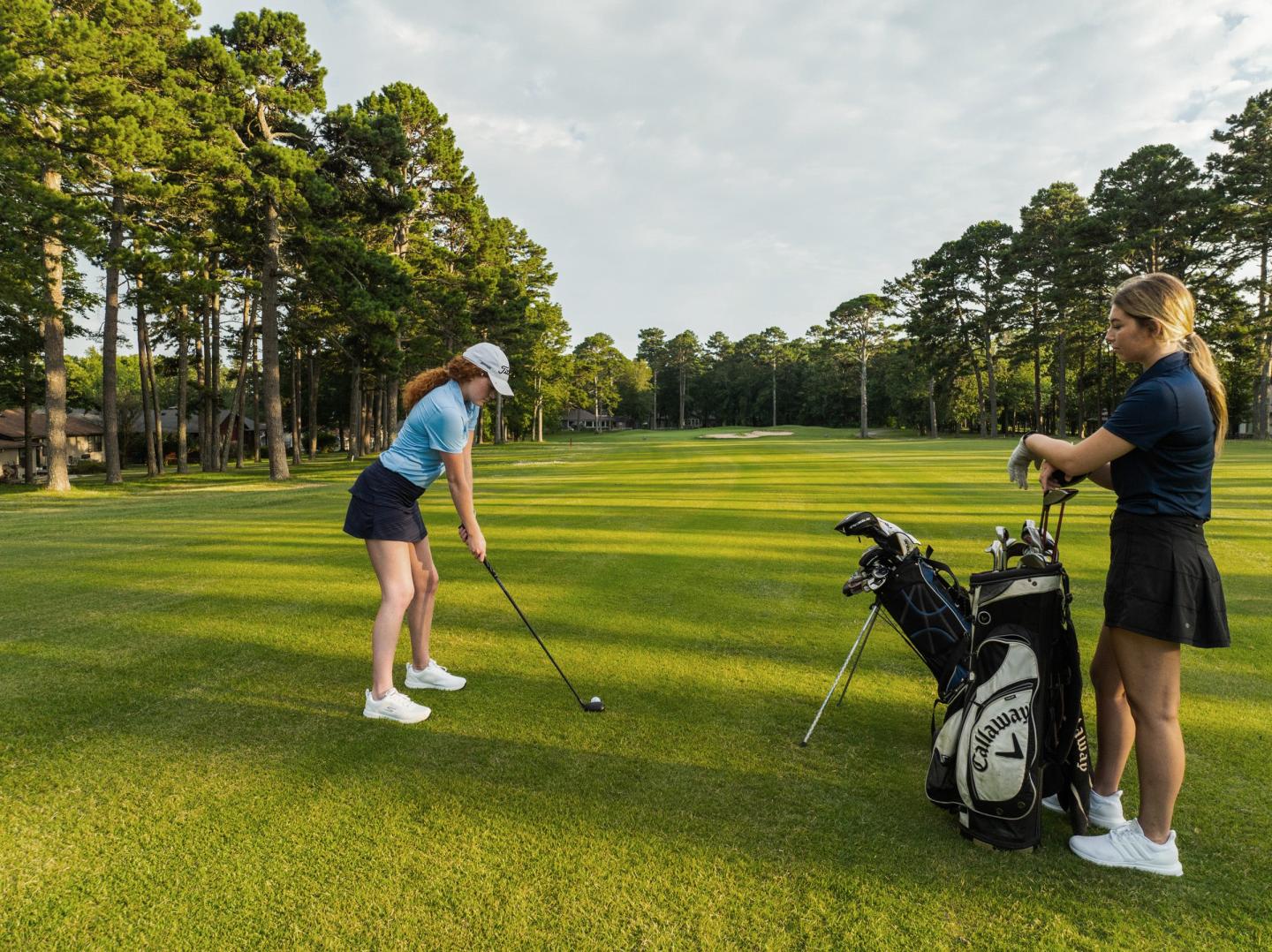 Golfer prepares to swing as another woman watches on a sunny green course.