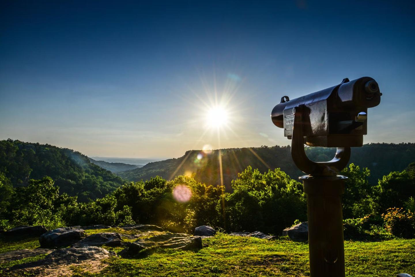 Coin-operated viewer overlooking a green valley at sunset.