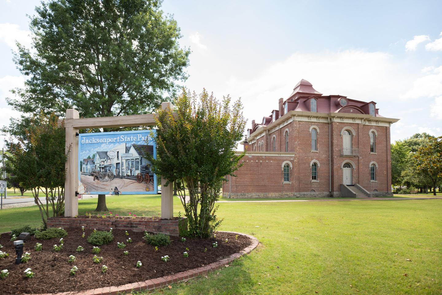 Historic brick building with a sign and green lawn under a blue sky.