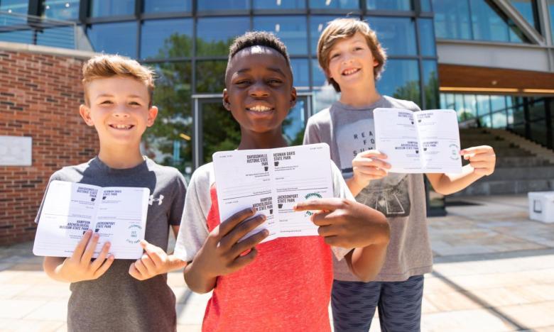 Three boys smiling, holding pamphlets outside a modern building.