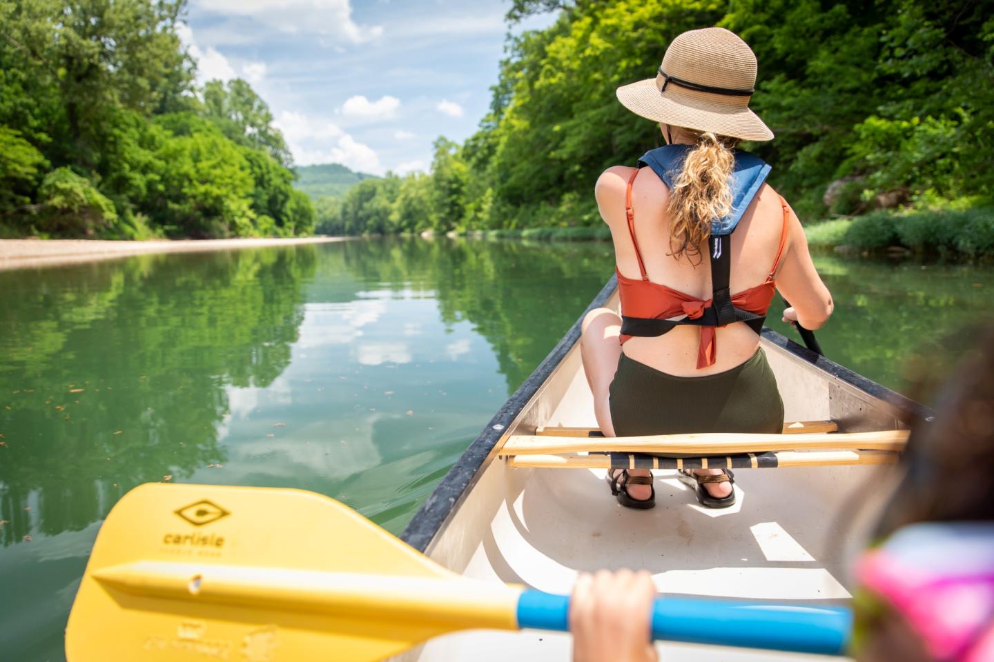 Canoeing on a calm river, surrounded by lush greenery, under a clear blue sky.