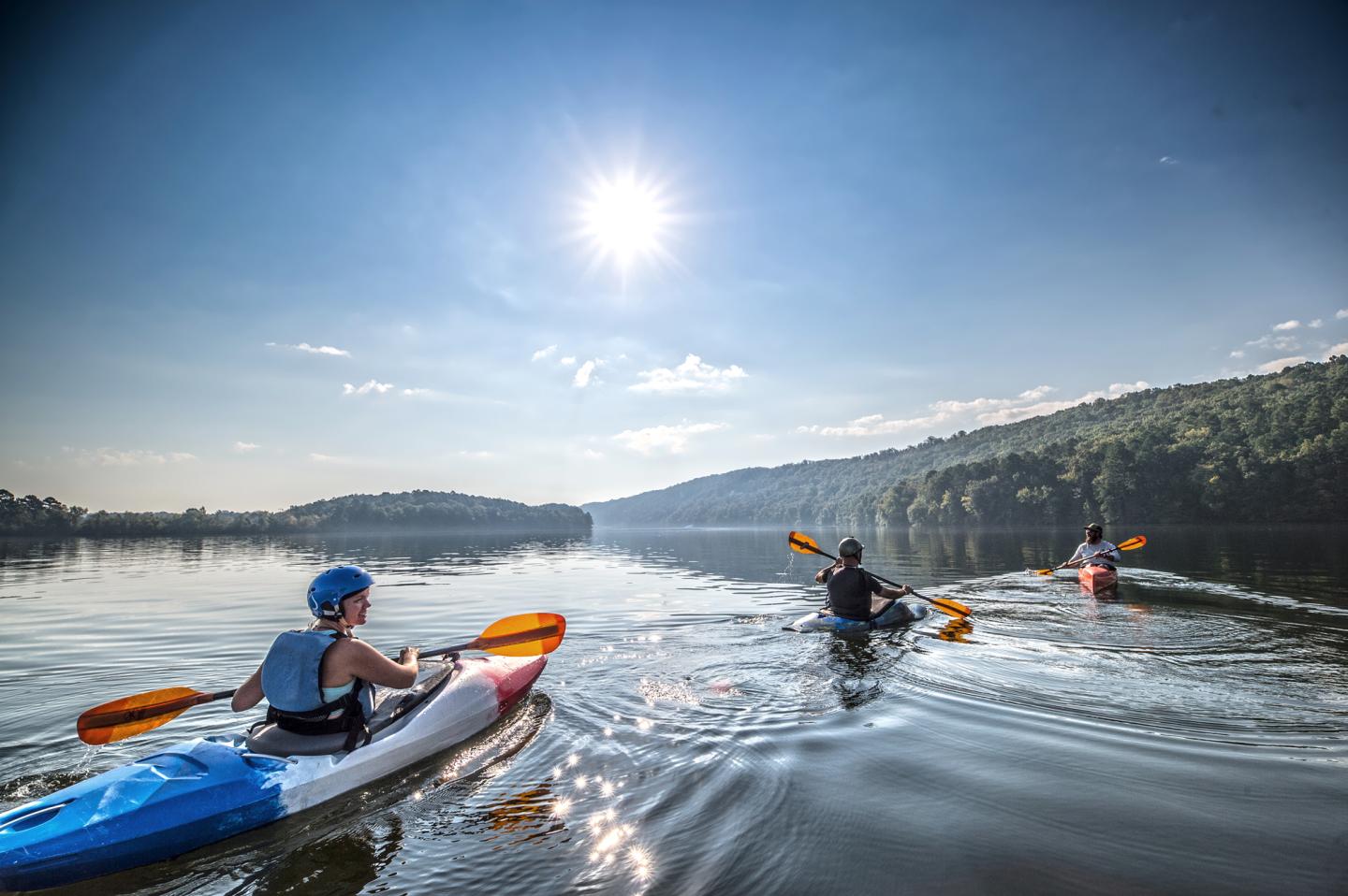 People kayaking on a calm lake under a bright sun.