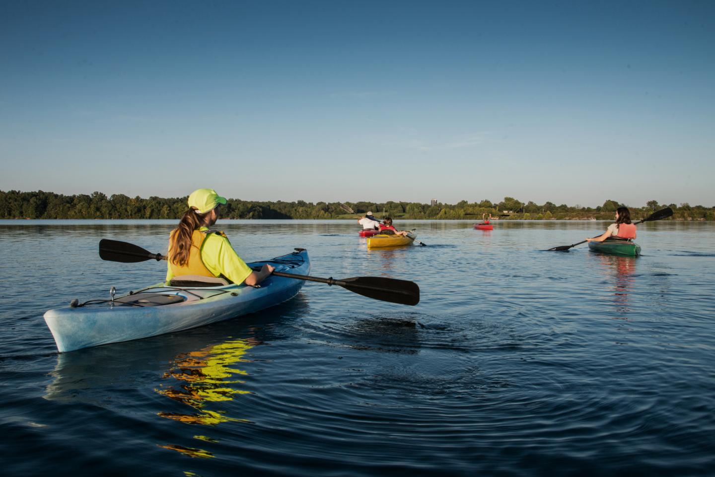 Kayakers paddling on a calm lake under a clear blue sky.