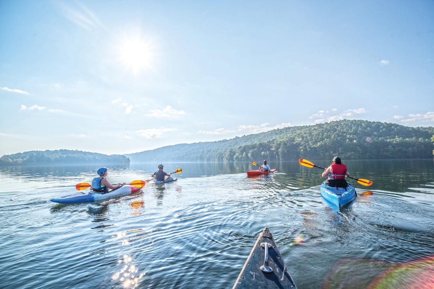 Kayakers paddling on a serene lake under a bright sun.