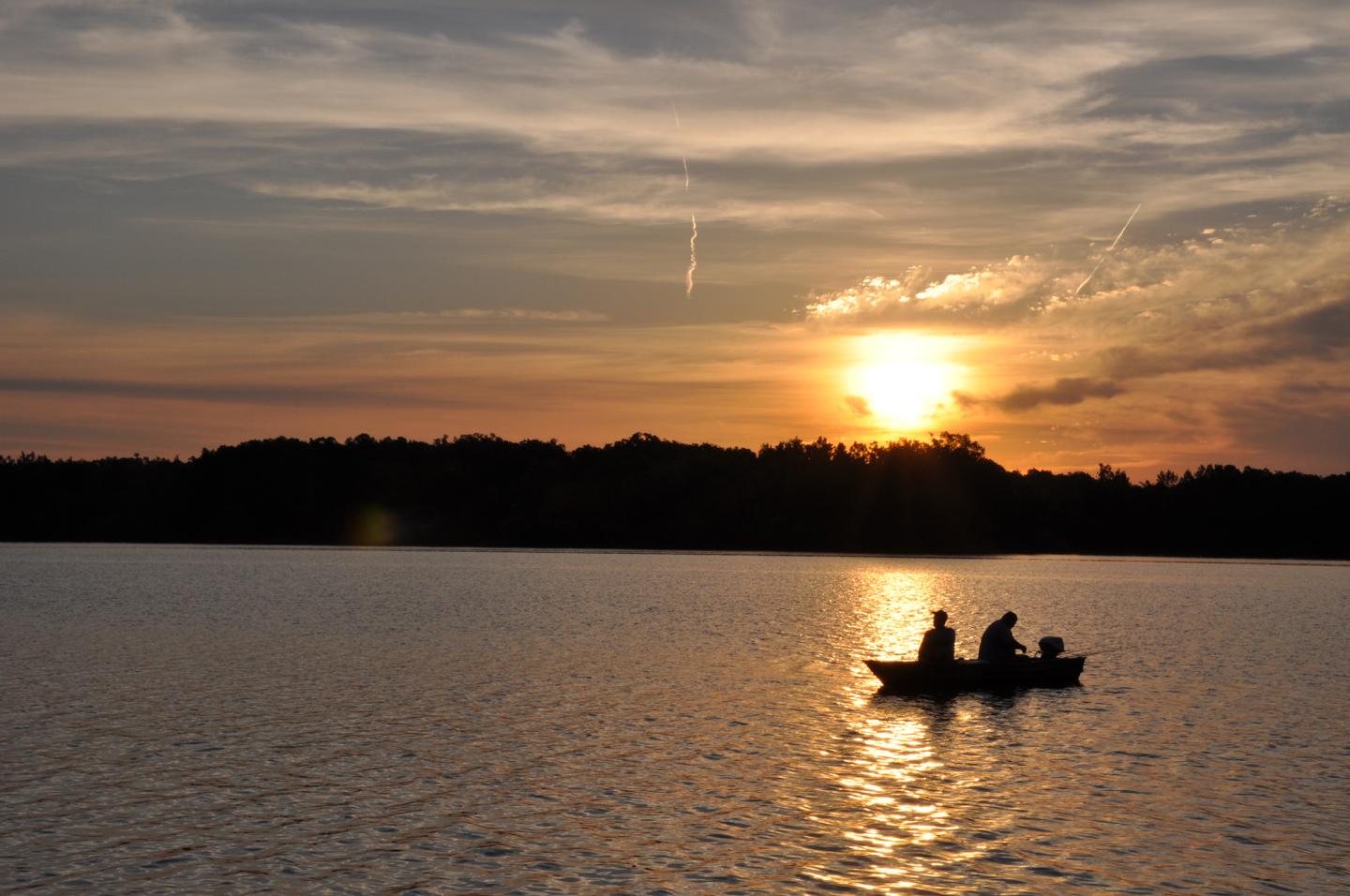 Silhouetted canoe on a lake at sunset, with orange sky and dark trees.