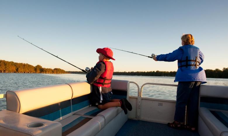 Child and adult fishing on a boat at sunset, with calm water and clear sky.