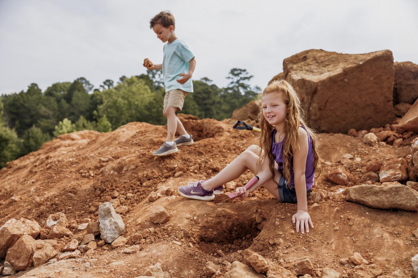 Children playing on a rocky hill, surrounded by trees.